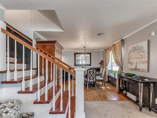 staircase with carpet flooring, ornate columns, a textured ceiling, crown molding, and a chandelier