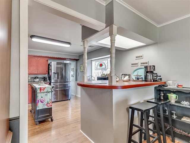 kitchen with kitchen peninsula, stainless steel fridge with ice dispenser, decorative columns, and a kitchen breakfast bar