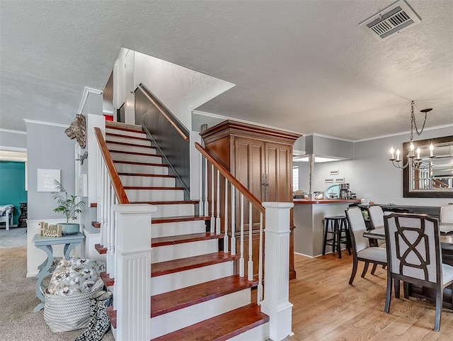 staircase with hardwood / wood-style flooring, an inviting chandelier, a textured ceiling, and ornamental molding