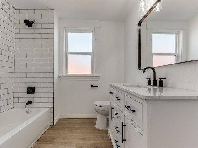 full bathroom featuring a wealth of natural light, toilet, hardwood / wood-style flooring, vanity, and tiled shower / bath