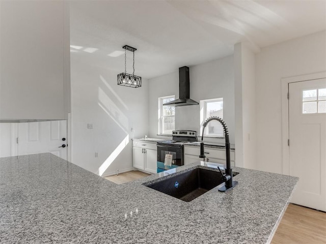 kitchen with light stone counters, sink, wall chimney range hood, pendant lighting, and stainless steel electric range oven