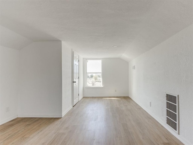 additional living space with a textured ceiling, light hardwood / wood-style flooring, and vaulted ceiling