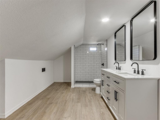 bathroom with a tile shower, wood-type flooring, a textured ceiling, toilet, and vanity