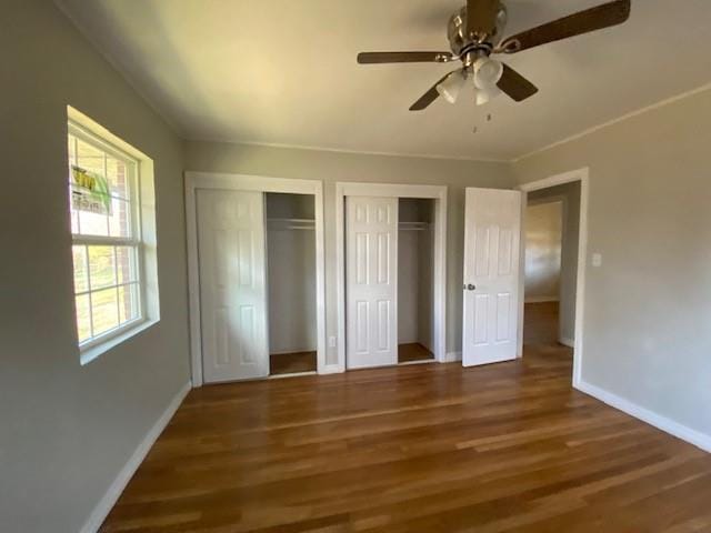 unfurnished bedroom with dark hardwood / wood-style floors, ceiling fan, and multiple closets