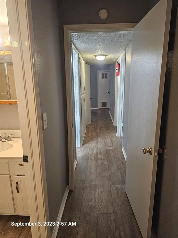 hall featuring a textured ceiling, dark wood-type flooring, and sink