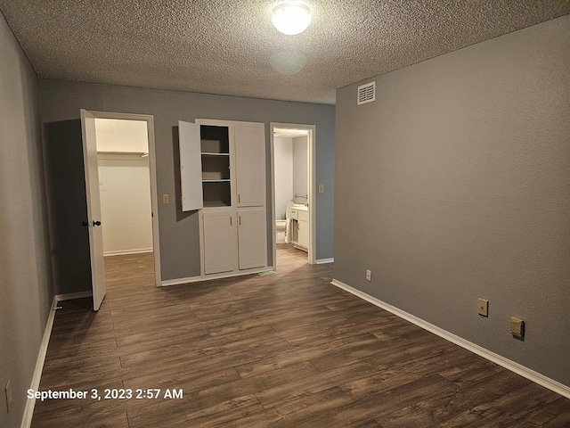 unfurnished bedroom featuring a textured ceiling, a spacious closet, a closet, and dark wood-type flooring