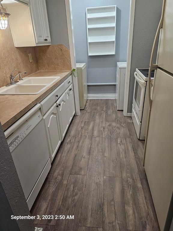 kitchen featuring white appliances, sink, hardwood / wood-style floors, white cabinetry, and washer / dryer