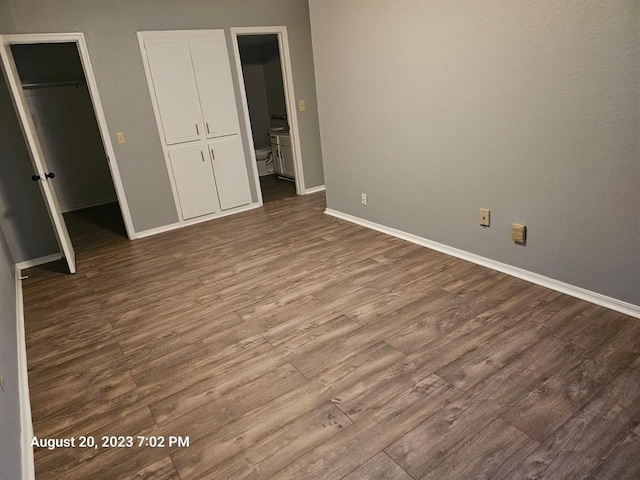 unfurnished bedroom featuring wood-type flooring, a walk in closet, connected bathroom, and a closet