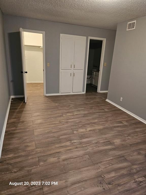 unfurnished bedroom with ensuite bathroom, dark hardwood / wood-style flooring, a spacious closet, and a textured ceiling