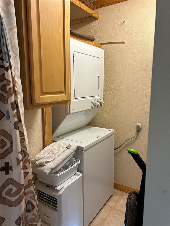 clothes washing area with cabinets and stacked washing maching and dryer