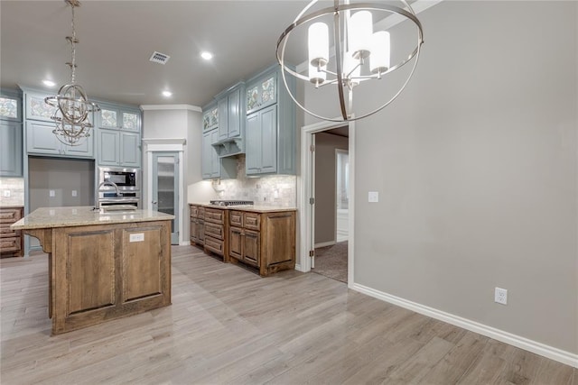 kitchen featuring sink, stainless steel appliances, light stone counters, backsplash, and a center island with sink