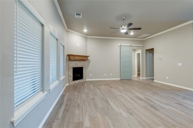 unfurnished living room with light wood-type flooring, ornamental molding, ceiling fan, a barn door, and a fireplace