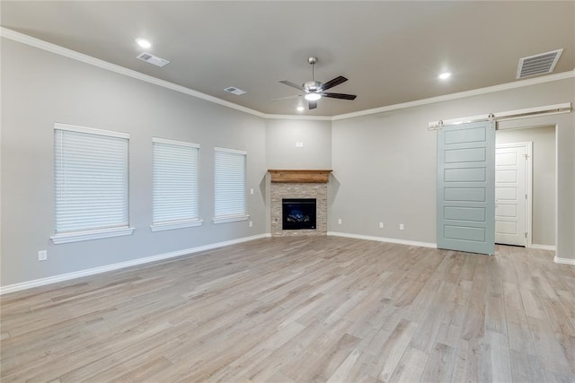 unfurnished living room featuring a barn door, light hardwood / wood-style flooring, a stone fireplace, and crown molding