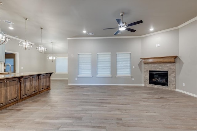 unfurnished living room featuring light wood-type flooring, ornamental molding, ceiling fan with notable chandelier, sink, and a fireplace