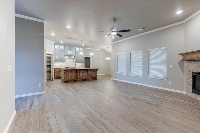 unfurnished living room with ceiling fan with notable chandelier, light hardwood / wood-style flooring, a stone fireplace, and crown molding