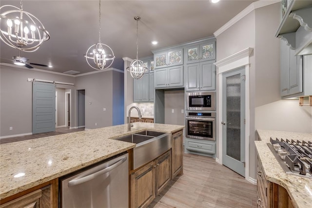 kitchen with light stone countertops, sink, stainless steel appliances, a barn door, and decorative light fixtures