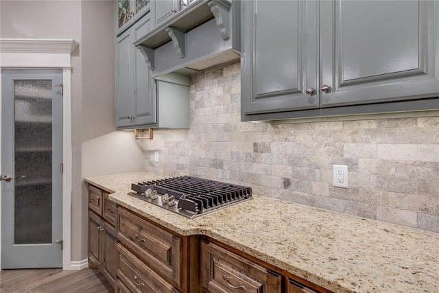 kitchen with hardwood / wood-style flooring, light stone counters, stainless steel gas cooktop, and gray cabinetry