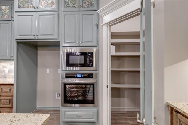 kitchen featuring hardwood / wood-style flooring, oven, light stone countertops, and built in microwave