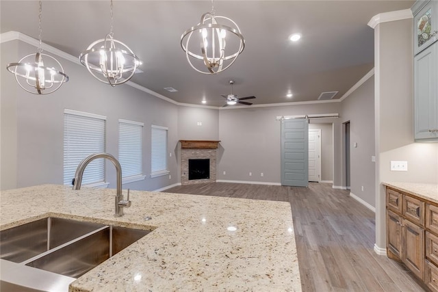 kitchen with ceiling fan, sink, light stone countertops, a barn door, and ornamental molding