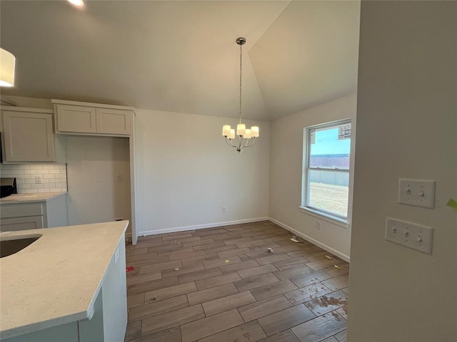 unfurnished dining area featuring lofted ceiling, wood finished floors, an inviting chandelier, and baseboards