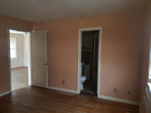 unfurnished bedroom featuring baseboards, wood finished floors, and ensuite bathroom