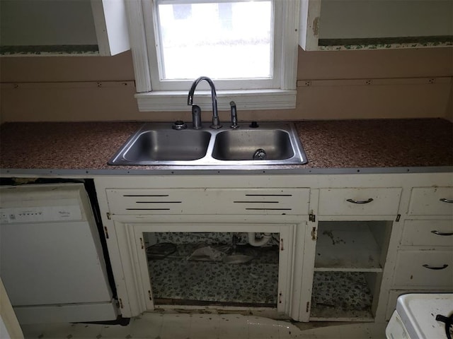 kitchen with dark countertops, white dishwasher, a sink, and white cabinetry