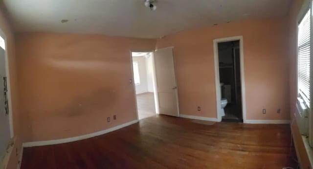 unfurnished bedroom featuring ensuite bath, multiple windows, baseboards, and wood finished floors