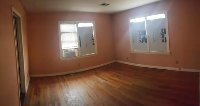 empty room with cooling unit, visible vents, baseboards, and wood finished floors