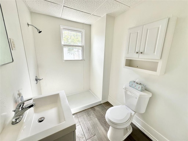 bathroom featuring a drop ceiling, toilet, sink, and walk in shower