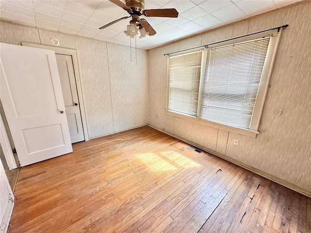 empty room with ceiling fan, wooden walls, and light hardwood / wood-style flooring