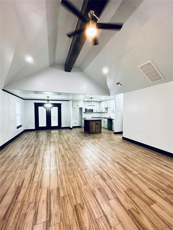 unfurnished living room featuring lofted ceiling with beams, ceiling fan, and light wood-type flooring