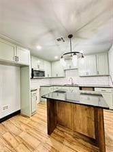 kitchen with white cabinetry, backsplash, pendant lighting, a kitchen island, and light wood-type flooring