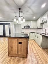 kitchen with backsplash, sink, decorative light fixtures, and light wood-type flooring