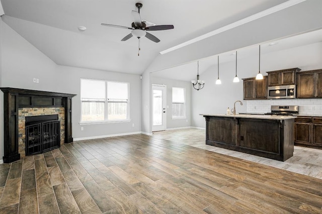 unfurnished living room with a fireplace, ceiling fan with notable chandelier, and vaulted ceiling