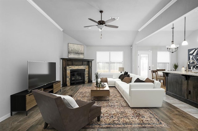 living room featuring ceiling fan with notable chandelier, a stone fireplace, sink, vaulted ceiling, and ornamental molding