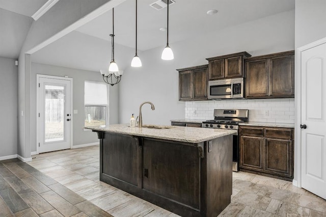 kitchen featuring appliances with stainless steel finishes, backsplash, dark brown cabinetry, pendant lighting, and an island with sink