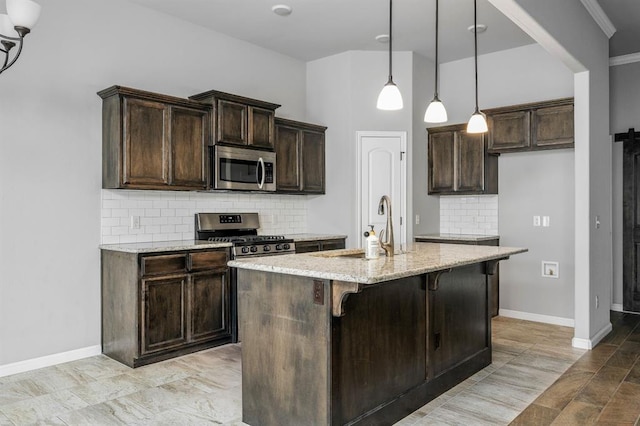 kitchen featuring appliances with stainless steel finishes, tasteful backsplash, light stone counters, a center island with sink, and hanging light fixtures