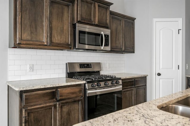 kitchen featuring decorative backsplash, light stone countertops, dark brown cabinets, and appliances with stainless steel finishes