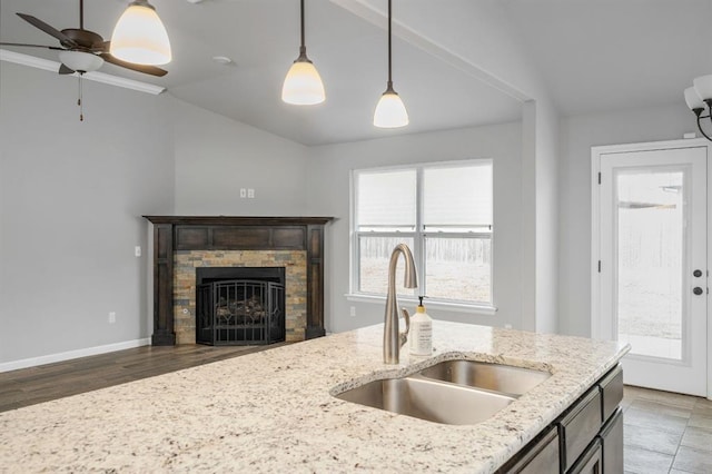 kitchen with light stone countertops, decorative light fixtures, vaulted ceiling, and sink