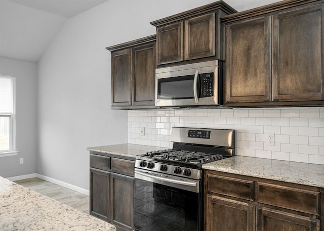 kitchen with dark brown cabinets, light stone counters, stainless steel appliances, and vaulted ceiling