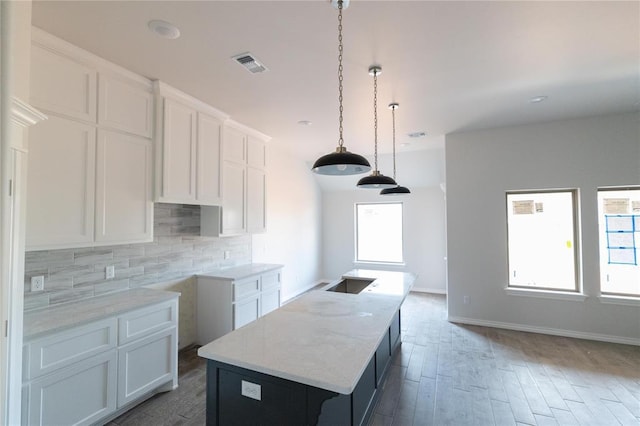 kitchen featuring tasteful backsplash, light stone counters, an island with sink, white cabinets, and visible vents