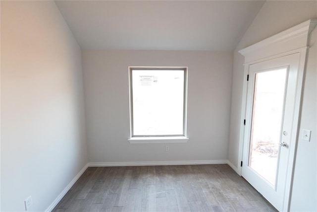empty room featuring lofted ceiling, light wood-style flooring, and baseboards