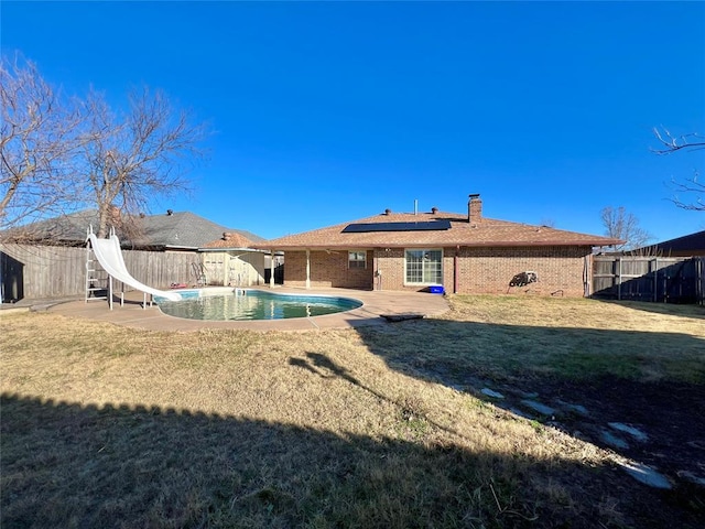 rear view of house with a fenced in pool, a lawn, a patio area, and solar panels