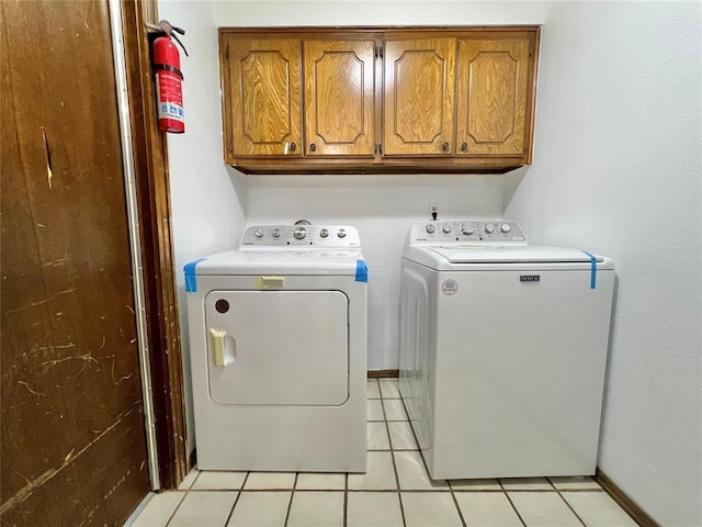 clothes washing area with light tile patterned flooring, cabinets, and washer and dryer