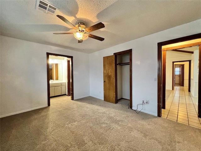 unfurnished bedroom featuring ensuite bath, light carpet, a textured ceiling, a closet, and ceiling fan