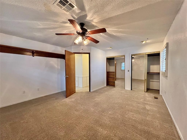 unfurnished bedroom featuring ceiling fan, two closets, light colored carpet, and a textured ceiling