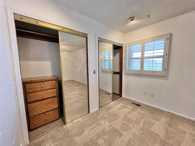 unfurnished bedroom featuring a textured ceiling, light carpet, and two closets