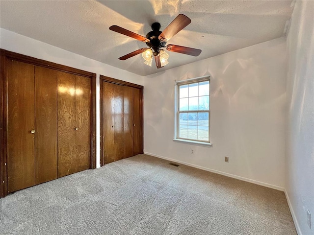 unfurnished bedroom with light carpet, ceiling fan, two closets, and a textured ceiling