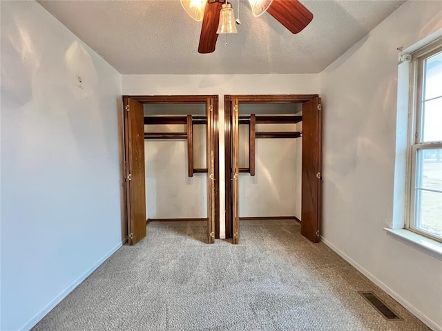 unfurnished bedroom with multiple closets, ceiling fan, light carpet, and a textured ceiling