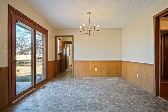 empty room featuring a textured ceiling, an inviting chandelier, and wooden walls